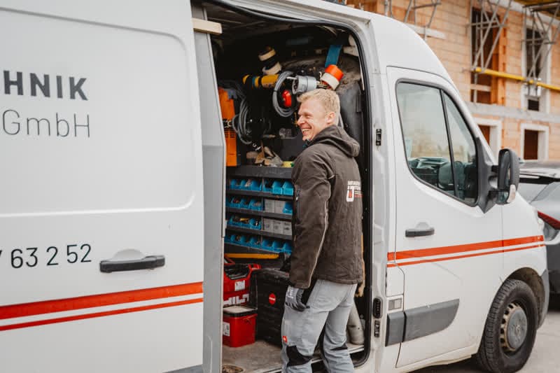 Monteur von Installationstechnik Wels steht lächelnd vor dem Firmenwagen